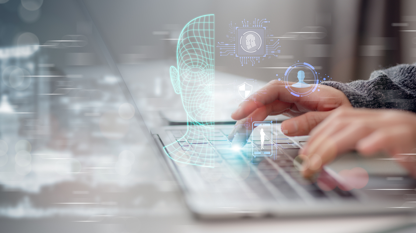 Hands typing on laptop with floating graphics of facial recognition and fingerprints